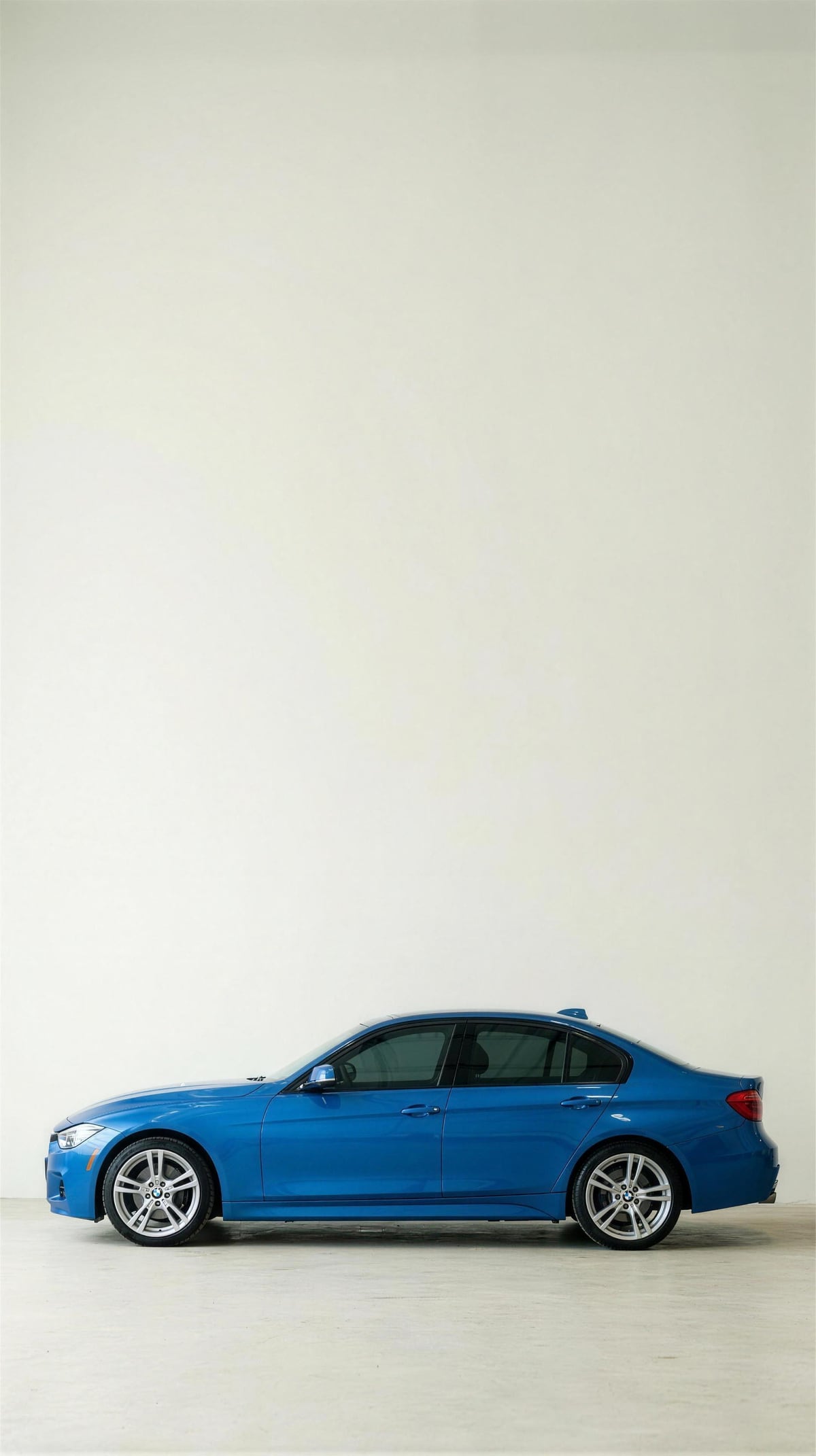 A blue BMW 3 Series sedan photographed in profile on a new set of tires